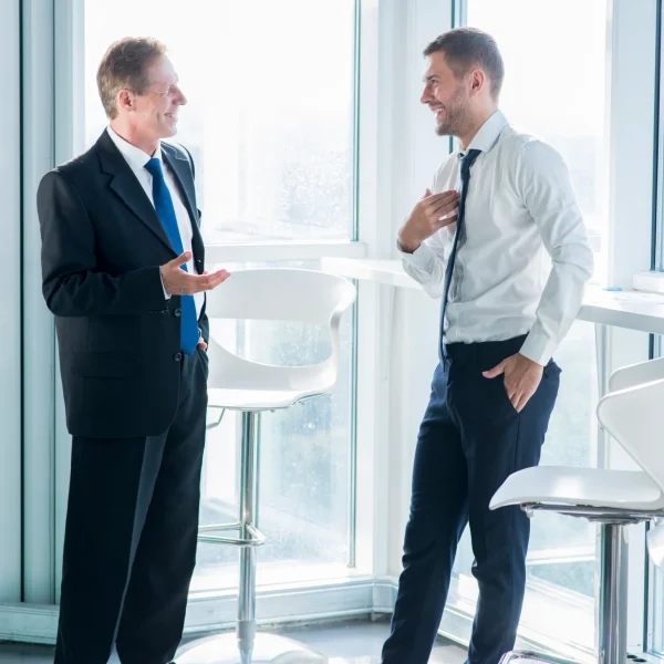 two-smiling-businessmen-standing-near-window-having-conversation-office